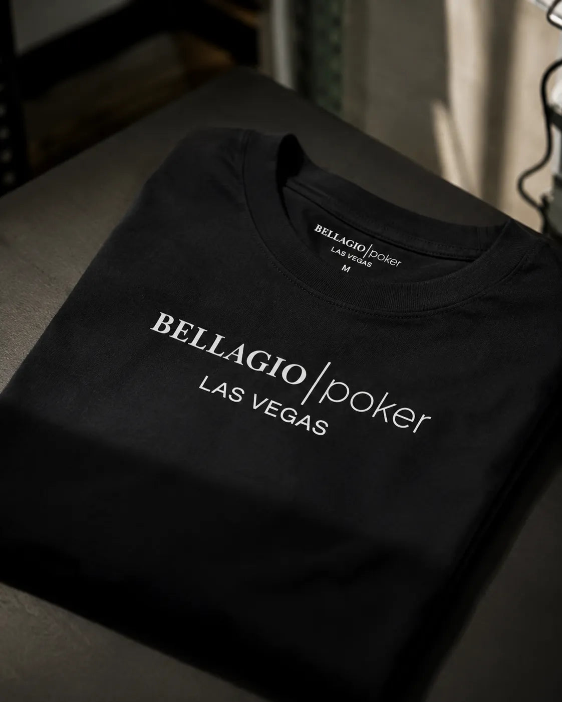 A folded black t-shirt with 'BELLAGIO | poker LAS VEGAS' printed in white text on the front, displayed on a dark surface.