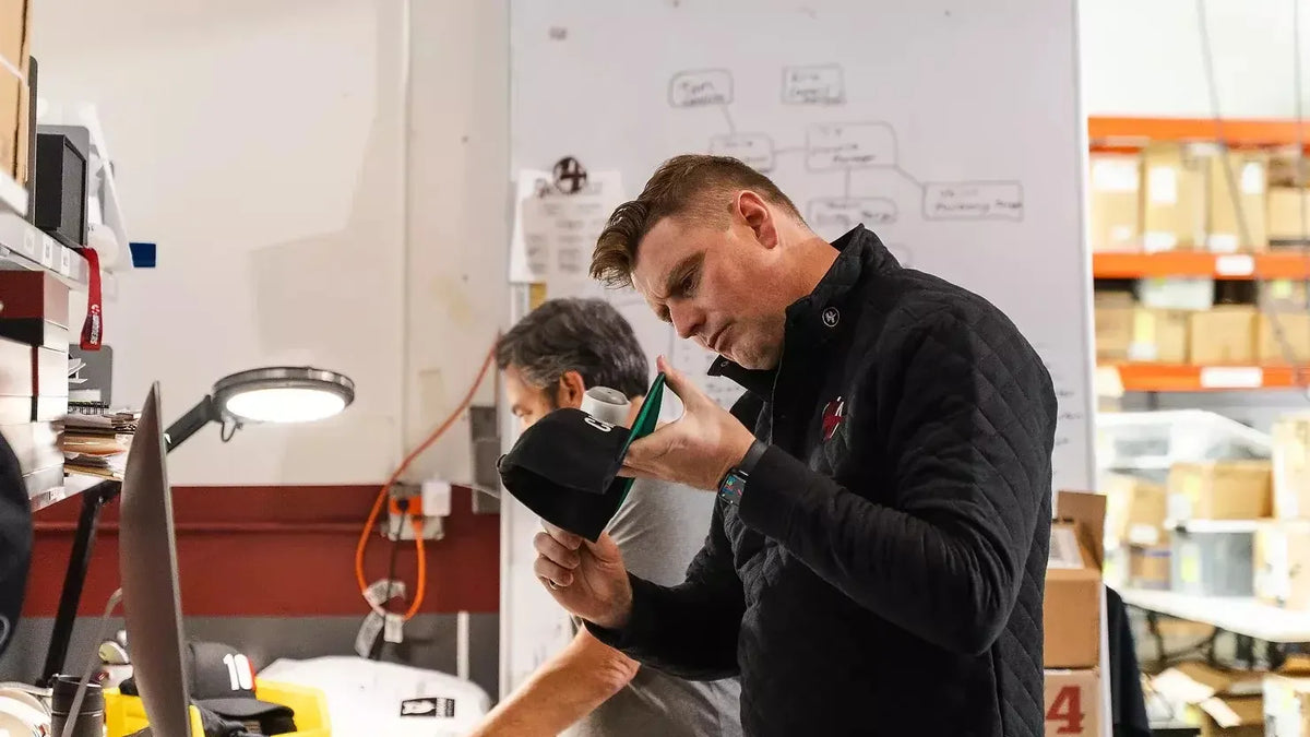 Two men in a workshop setting, one holding a helmet and the other looking at it.